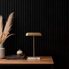 a small table with a lamp and some plants on it next to a black wall