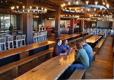 people sitting at tables in a restaurant with wooden benches and bar stools around them