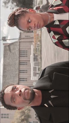 two young men standing next to each other in front of a tall building and trees