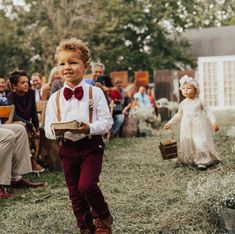 a little boy in a bow tie and suspenders walking down the aisle at a wedding