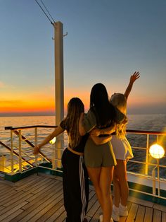 three women are hugging on the deck of a cruise ship at sunset, with their arms around each other