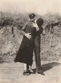 an old black and white photo of two people hugging each other in front of a dirt hill