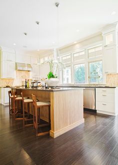 a large kitchen with wooden floors and white cabinetry on the walls, along with two bar stools