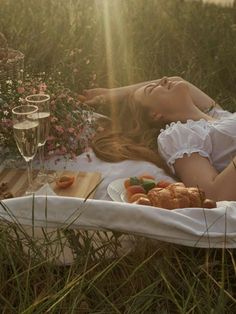 a woman laying on a blanket in the grass with food and drinks next to her