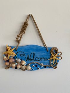 a welcome sign with shells and starfish hanging from a rope against a white wall