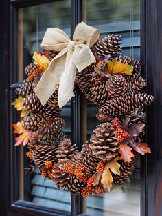 a wreath made out of pine cones and leaves with a bow on the front door