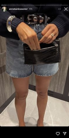 a woman in shorts and heels is holding a black purse with her right hand on the wallet