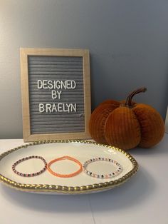 a white plate topped with two bracelets next to a framed sign that says designed by braehn