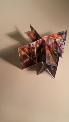 an origami bird made out of magazine pages on a table with the shadow coming from it