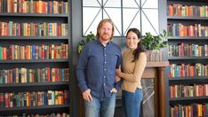 two people standing next to each other in front of bookshelves with many different colored books