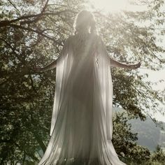 a woman dressed in white standing under a tree