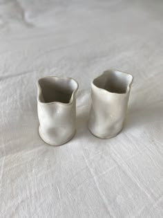 two white vases sitting on top of a white table cloth covered bedding area