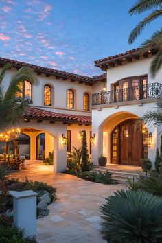 a large white house with lots of windows and palm trees in the front yard at dusk