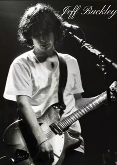 black and white photograph of a young man playing an electric guitar in front of a microphone