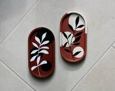 two red trays with black and white designs on them sitting on a tile floor