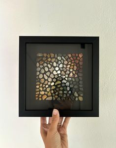 a hand holding up a framed photograph with rocks in it's center and bottom