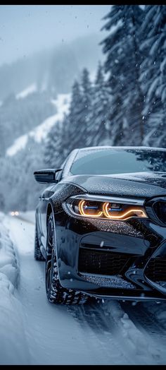 a car driving down a snow covered road in the middle of winter with headlights on