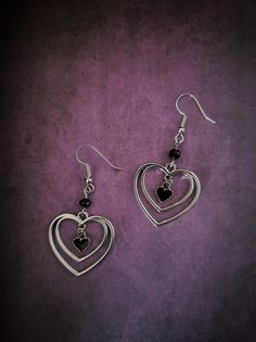 Introducing our stunning silver hollowed heart with black heart dangle earrings! These exquisite earrings are the perfect accessory to add a touch of elegance to any outfit. The intricate silver hollowed heart design is beautifully complemented by the dangling black heart, creating a unique and eye-catching look. Made with high-quality materials, these earrings are not only stylish but also lightweight and comfortable to wear all day long. Whether you're attending a special event or looking to elevate your everyday style, these silver hollowed heart with black heart dangle earrings are the perfect choice. Order now to add a little love and sophistication to your jewelry collection! Each product is one of a kind so there might be slight variations in colour, thickness, or shape. No two are Cute Black Earrings, Sterling Silver Earrings Dangle, Dark Feminine Earrings, Heart Jewelry Silver, Elegant Stainless Steel Heart Earrings, Metal Heart Beaded Earrings For Gifts, Metal Heart Beads Earrings For Gifts, Heart Beads Metal Earrings For Gift, Gift Metal Heart Earrings With Heart Beads