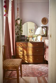 a bedroom with a dresser, mirror and chair next to a window in the room