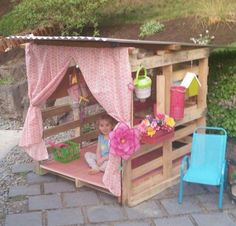 a child's play house made out of pallet wood with pink curtains and flowers