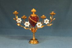 a golden candelabra with white flowers on it and a red glass vase