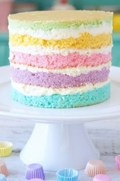 a multi - colored cake on a white plate with cupcakes around it and in the background