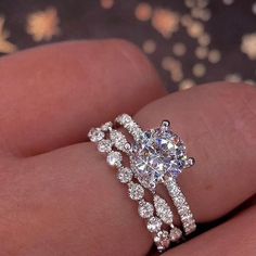 a woman's hand with a diamond ring on top of her finger and the other hand holding an engagement ring