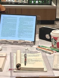 an open laptop computer sitting on top of a table covered in books and writing utensils