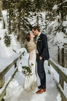 a bride and groom kissing on a bridge in the snow