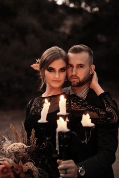 a man and woman standing next to each other with candles in front of their faces