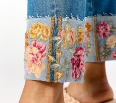 a woman's feet with floral embroidered jeans and sandals on top of her legs