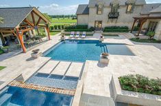 an outdoor swimming pool surrounded by stone patios and seating areas with chairs around it