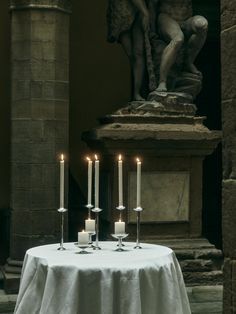 candles are lit on a table in front of a statue with a kneeling figure behind it