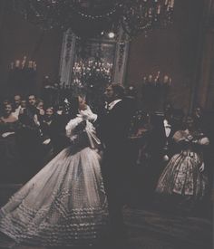 a man and woman in formal dress standing next to each other near a chandelier