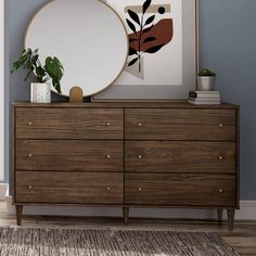 a wooden dresser topped with a mirror and potted plant next to a blue wall