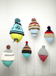 several knitted hats are on sticks in front of a white wall and one has a moustache