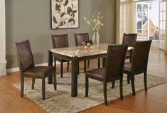 a dining room table with chairs and a vase on the rug in front of it