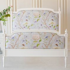 a white bed with flowers on it next to a potted plant and wallpaper