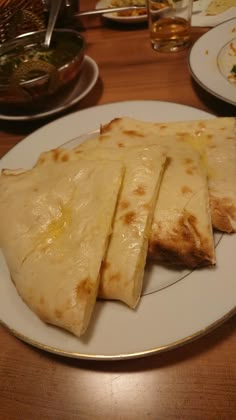 four quesadillas on a white plate sitting on a wooden table with silver trim