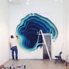 a man standing in front of a painting on the side of a white wall next to a ladder