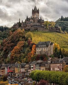 an old castle on top of a hill surrounded by trees and other small town buildings