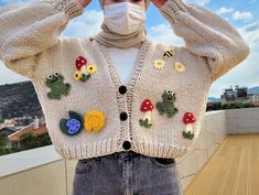 a woman wearing a white sweater with crocheted frog appliques on it