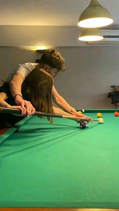 two people are playing pool in a room with green table and lights on the ceiling