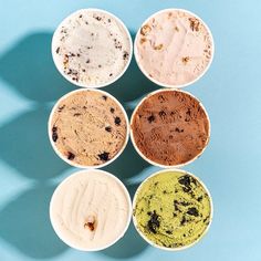 six different colored ice creams in white bowls on a blue background with shadows from the top