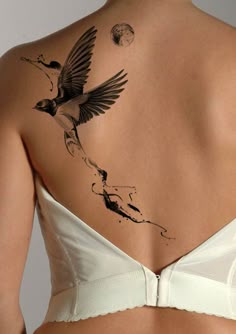 the back of a woman's bra with a bird tattoo on her left side