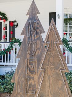 two wooden christmas trees sitting in front of a house with holiday decorations on the porch