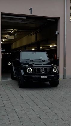 a black mercedes benz is parked in front of a garage with its doors open and the lights on