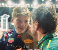 two men talking to each other in front of a crowd at a sporting event with lights on