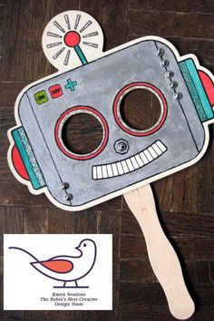 a paper cut out of a robot with a bird on it's head and a wooden spoon in the foreground