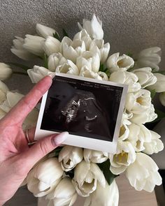 a person holding an electronic device in front of some white flowers and tulips